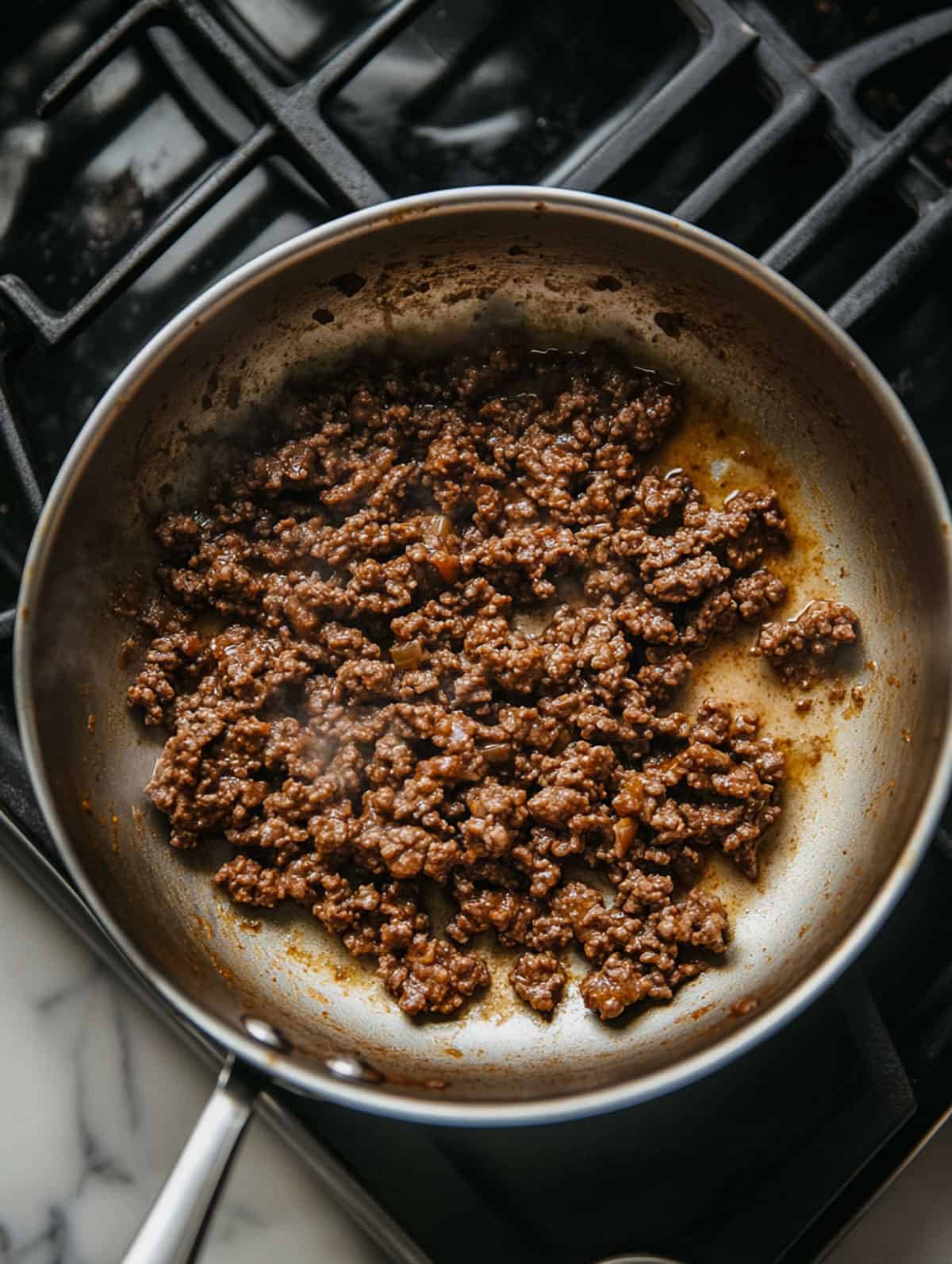 Ground beef browning in a skillet on a stovetop.