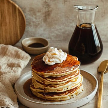 Stack of brown sugar protein pancakes topped with whipped cream and a drizzle of syrup on a ceramic plate