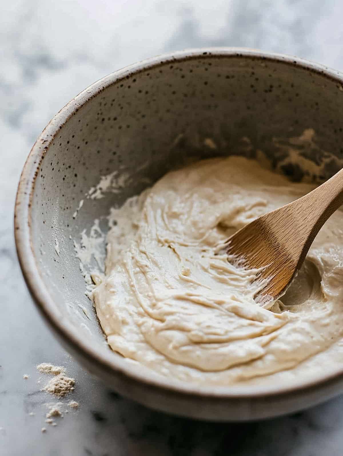 Thick brown sugar protein pancake batter in a ceramic bowl being mixed with a wooden spoon.