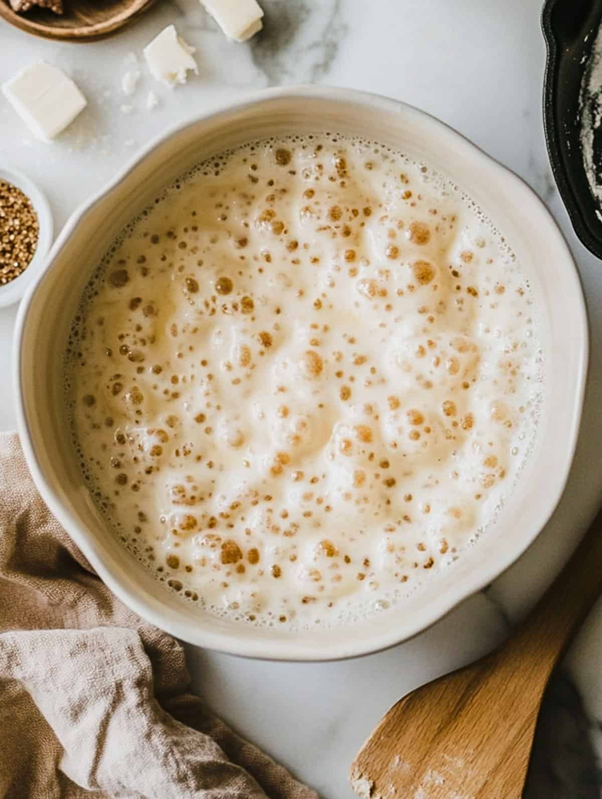 Close-up of bubbly brown sugar protein pancake batter in a mixing bowl with ingredients on the side