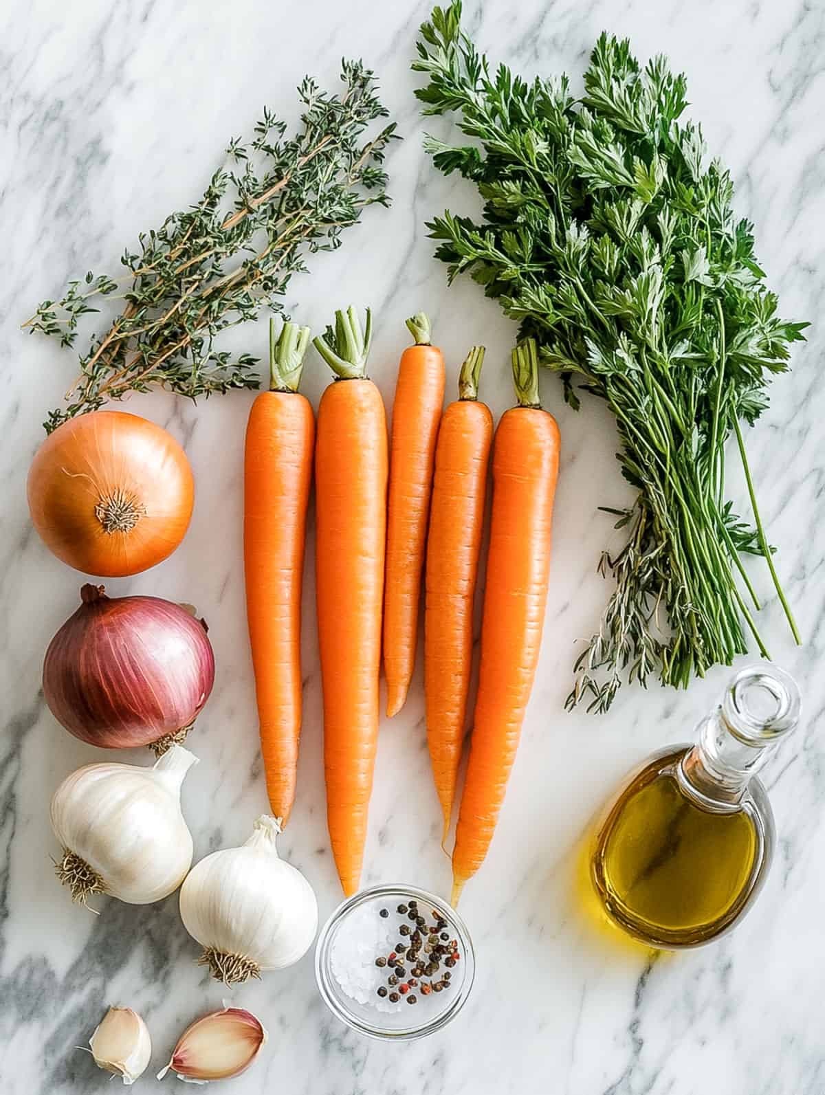 Whole carrots, onions, garlic, thyme, parsley, olive oil, and peppercorns neatly arranged on a marble counter.