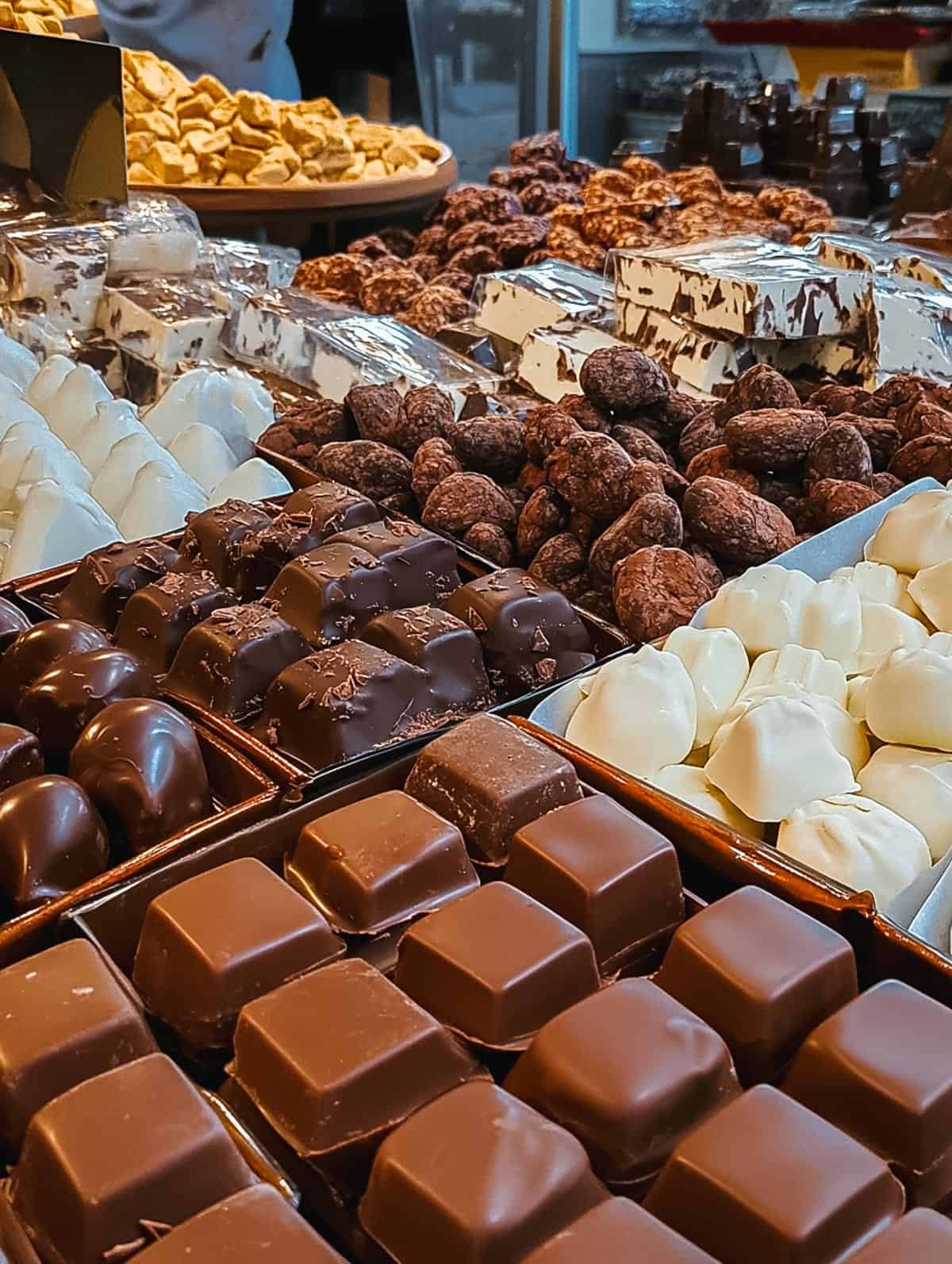 A beautifully arranged selection of luxury chocolates, showcasing various types of truffles and bonbons. The assortment includes chocolates with smooth, glossy finishes in dark, milk, and white varieties, with decorative toppings like swirls and nuts.