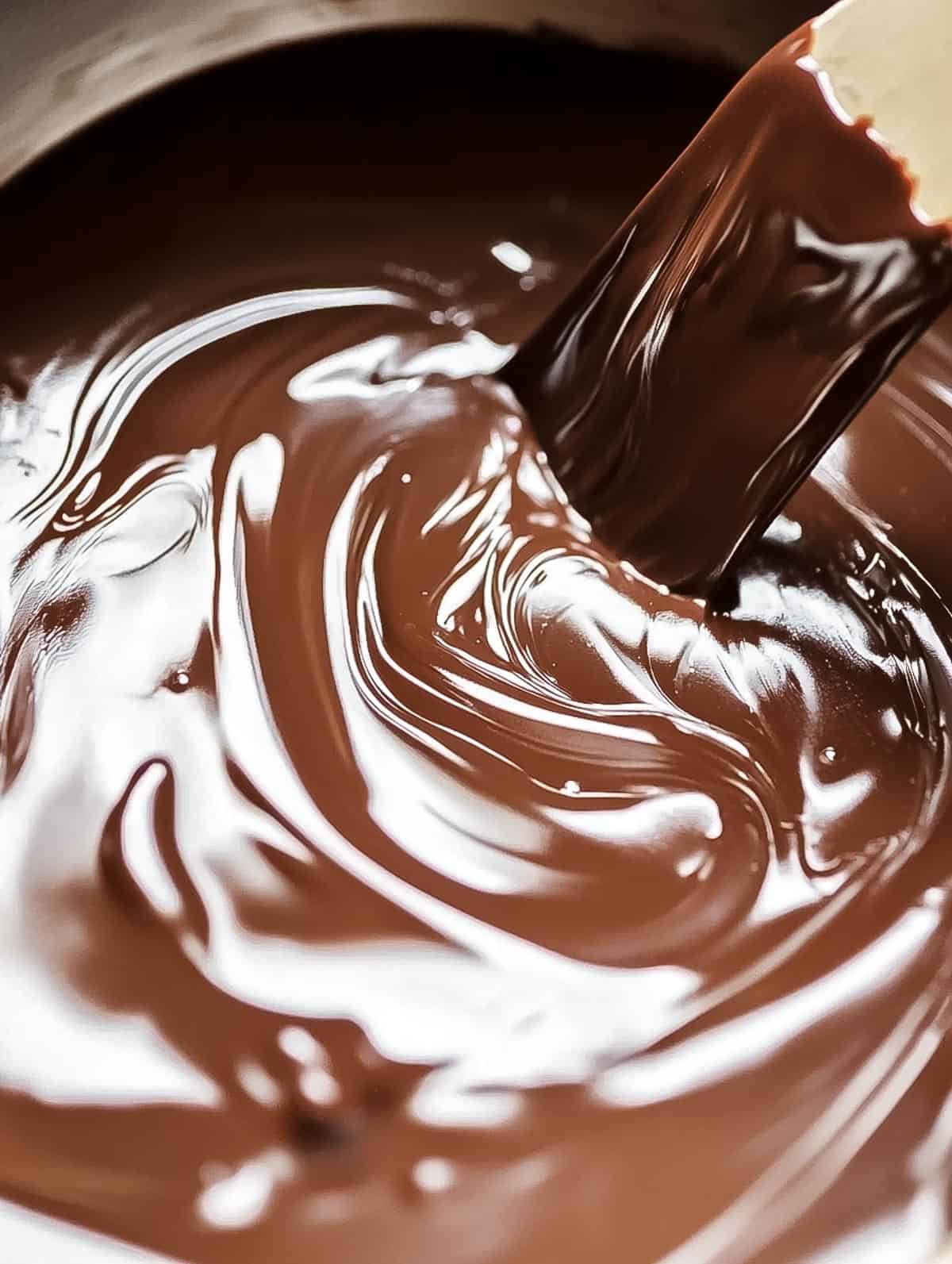 Swirls of melted chocolate in a mixing bowl being stirred.