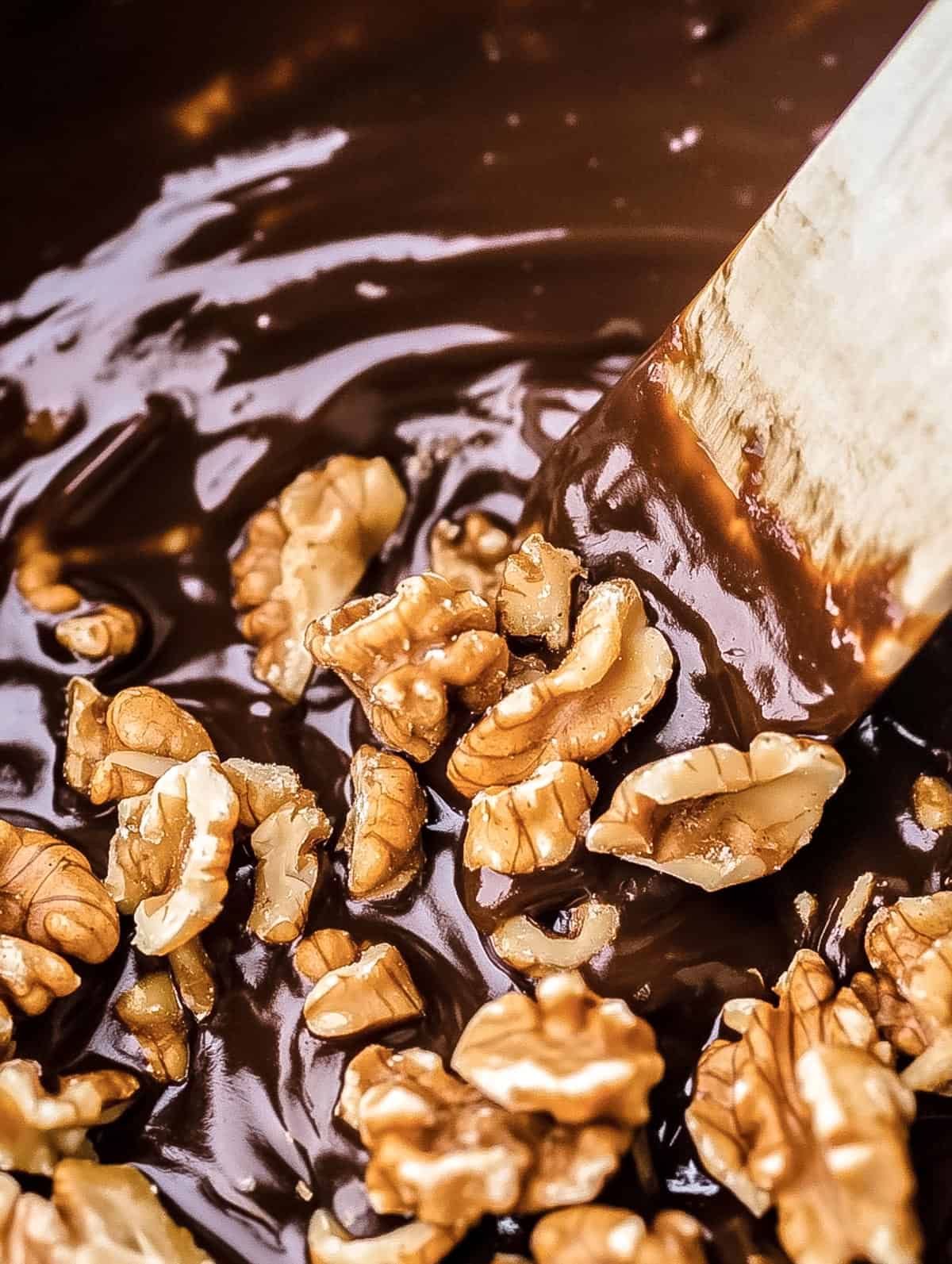 Roasted walnuts being stirred into melted chocolate fudge mixture.