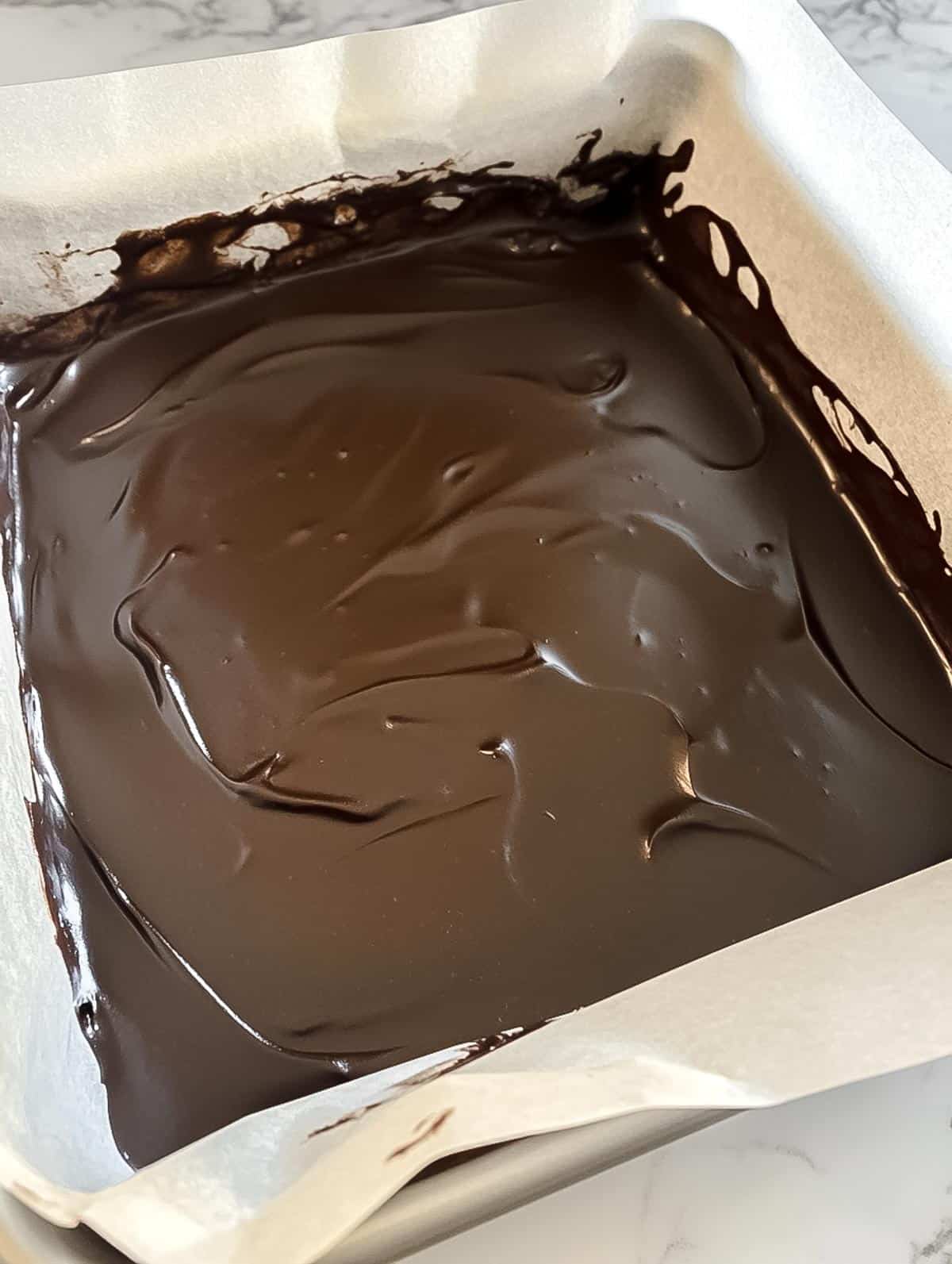 Chocolate fudge spread evenly in a parchment-lined baking pan.