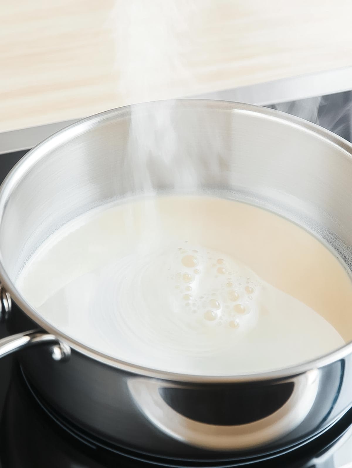 Cream heating in a saucepan, gently bubbling on the stove.