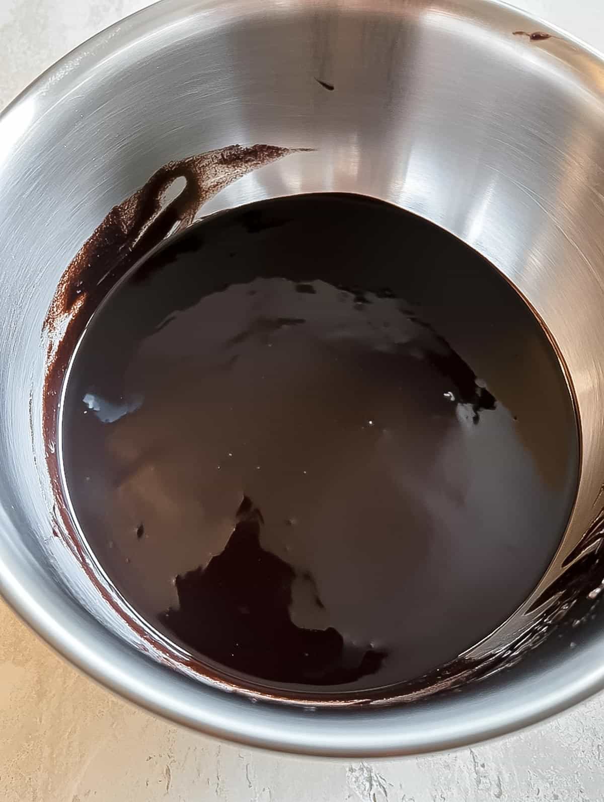 Melted chocolate cooling in a metal mixing bowl.