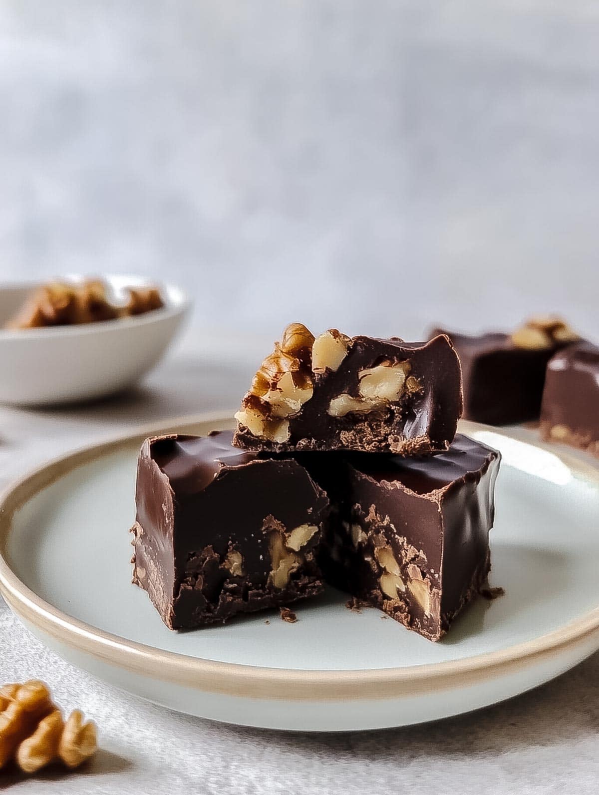 Chocolate walnut fudge stacked on a plate, showing walnut pieces inside.