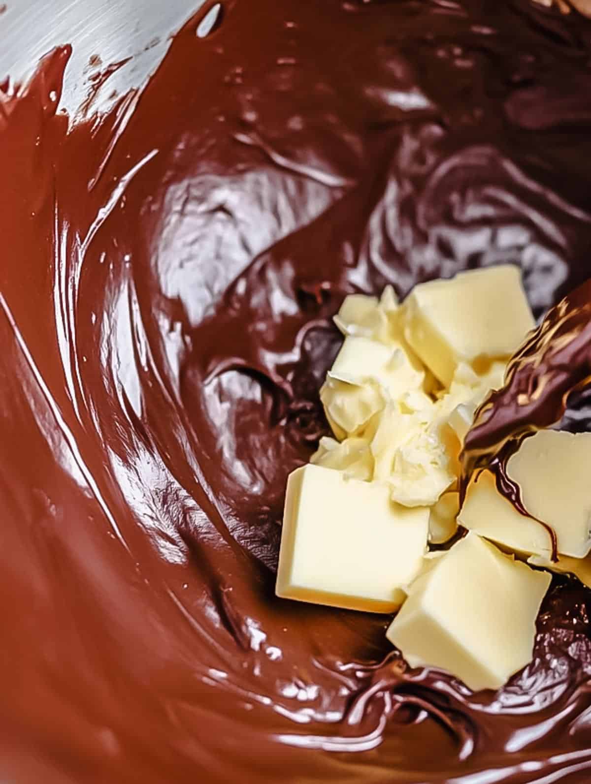 Chopped butter being added to melted chocolate in a mixing bowl.