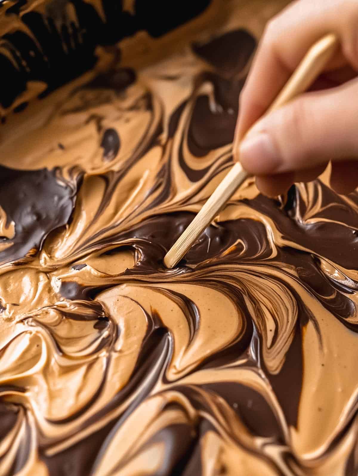 Hand swirling chocolate and gingerbread fudge with a toothpick.