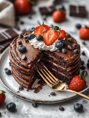 Sliced chocolate protein pancakes topped with berries, whipped cream, and chocolate chips.