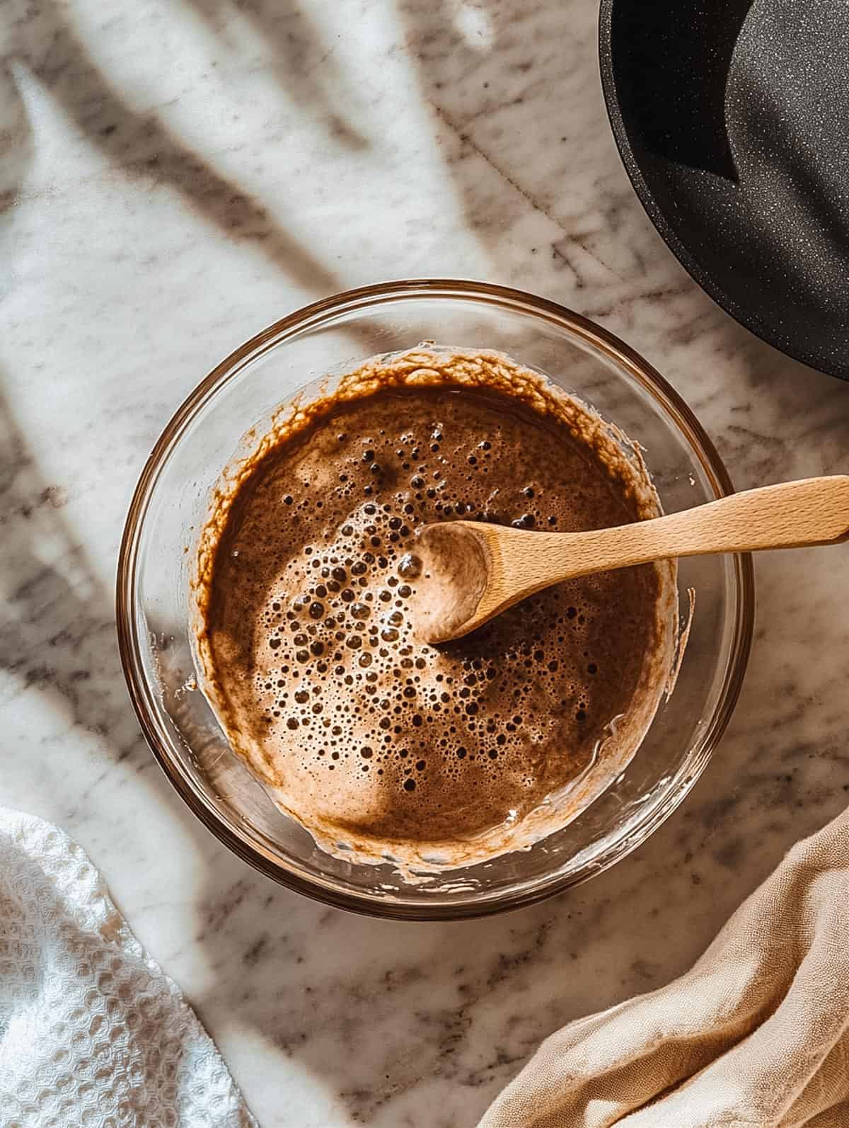 Glass bowl with chocolate pancake batter being stirred with a wooden spoon.