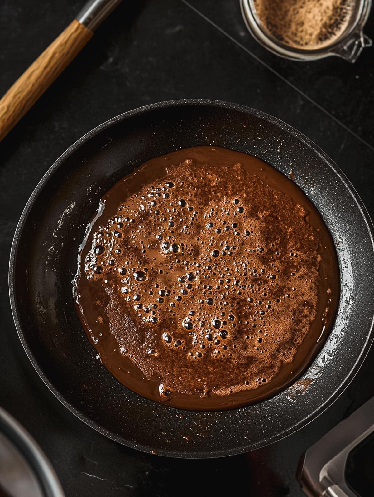 Chocolate protein pancake batter bubbling in a non-stick skillet.