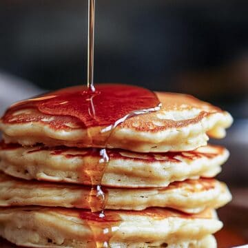 Maple syrup being poured over a stack of fluffy pancakes