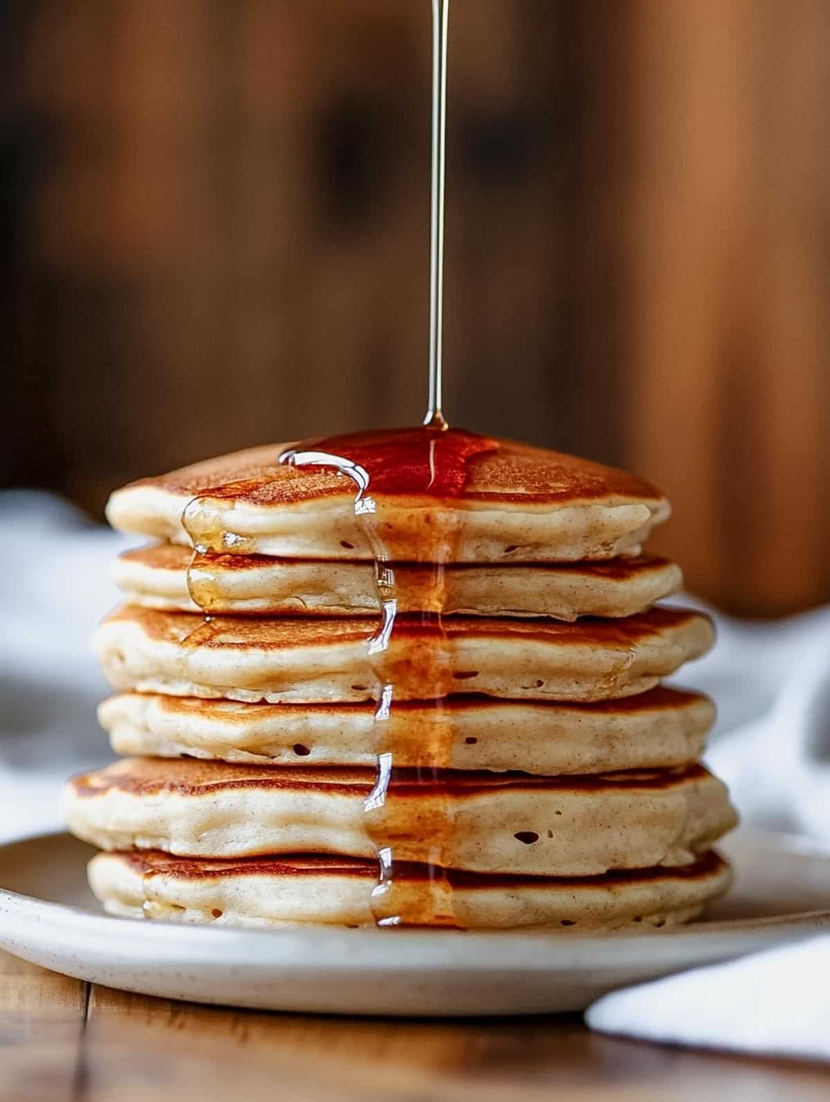 Close-up of protein pancakes with maple syrup being drizzled from above.