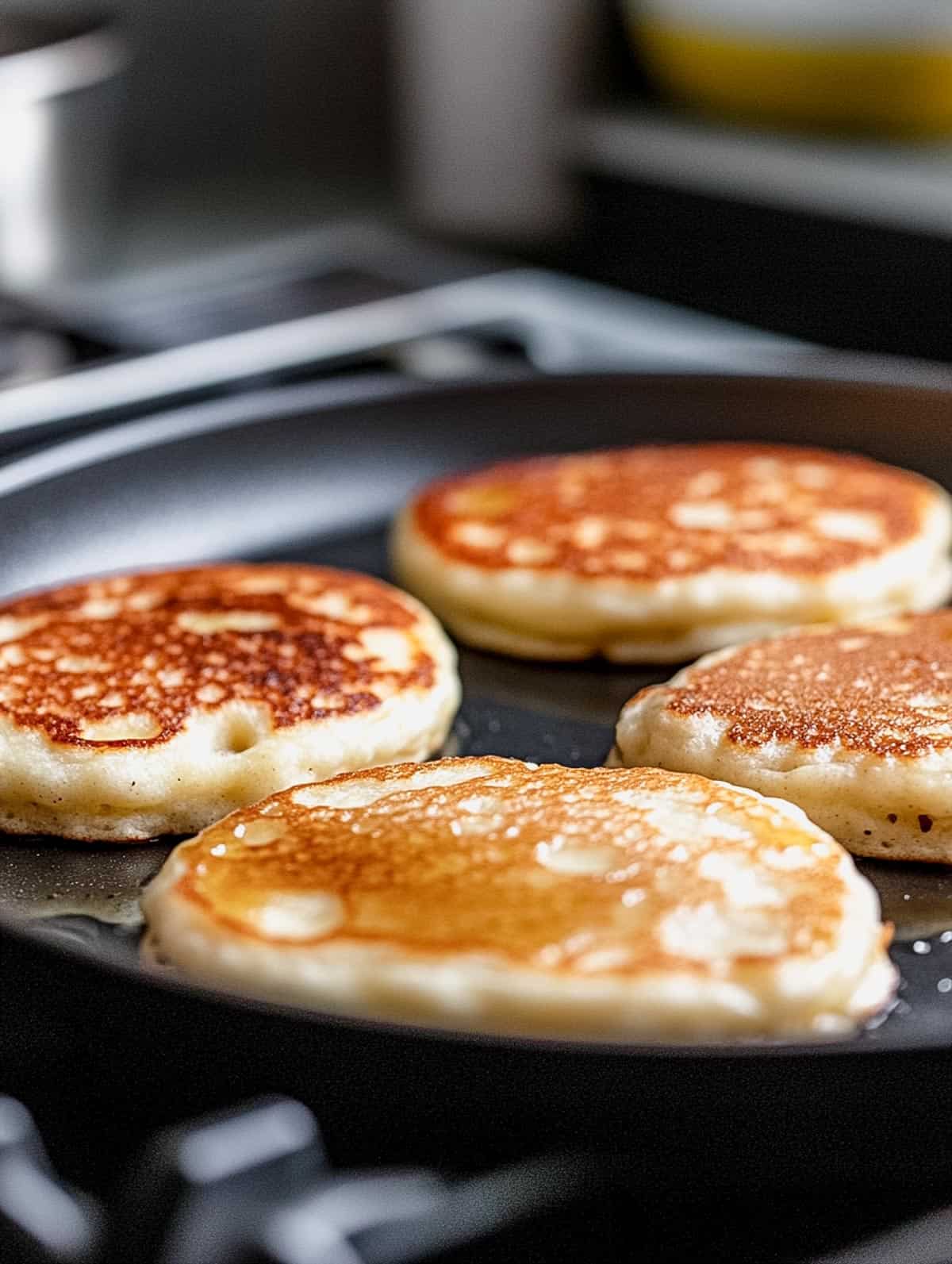 Four protein pancakes cooking on a skillet, with bubbles forming on the surface, ready to flip.