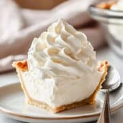 A slice of pie topped with a generous swirl of fresh whipped cream, served on a white plate with a spoon.