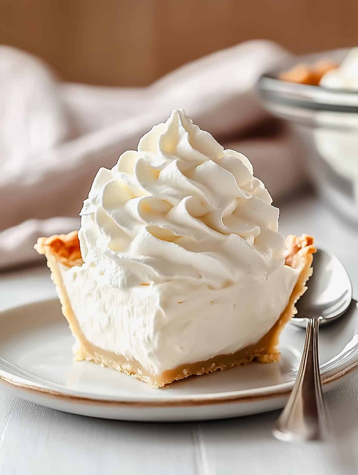 A slice of pie topped with a generous swirl of fresh whipped cream, served on a white plate with a spoon.