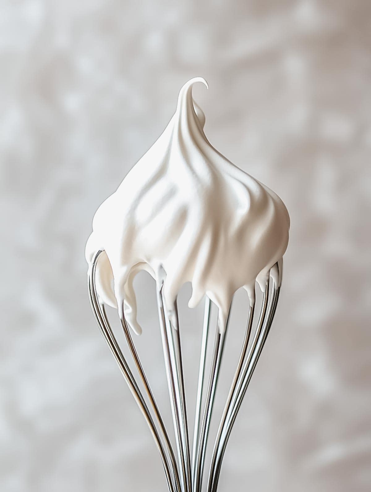 Soft peaks of whipped cream forming on a metal whisk, showing the smooth, airy texture of freshly whipped cream.