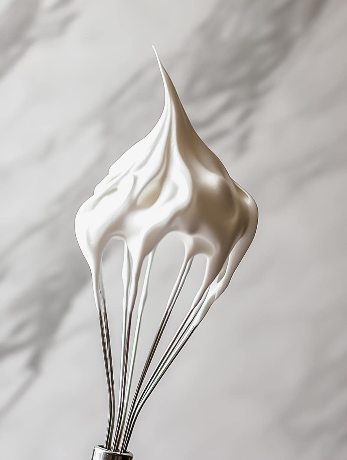 A close-up of stiff peaks of whipped cream on a whisk, showing the smooth and firm texture of perfectly whipped cream.