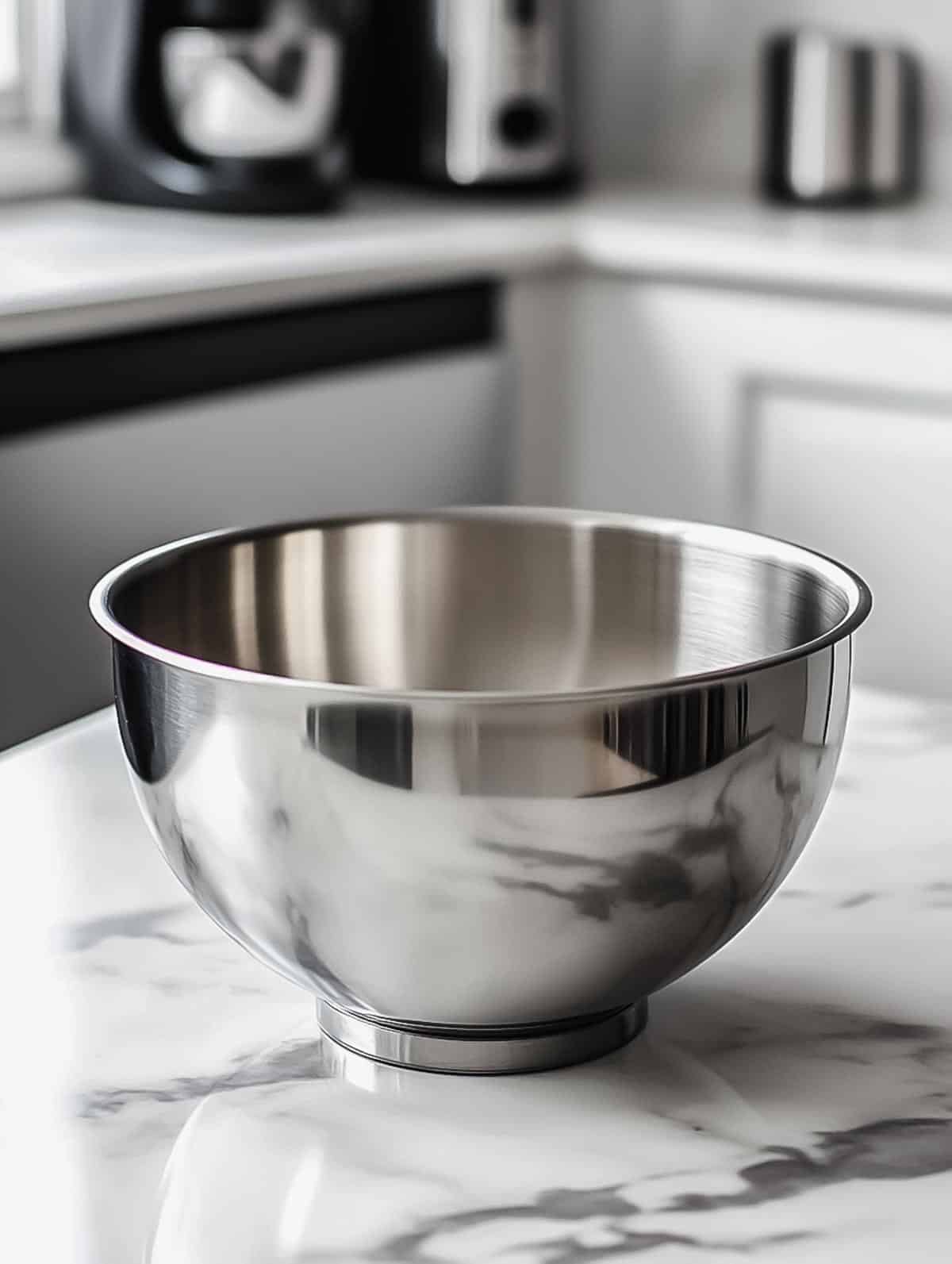 A stainless steel mixing bowl placed on a marble kitchen countertop.