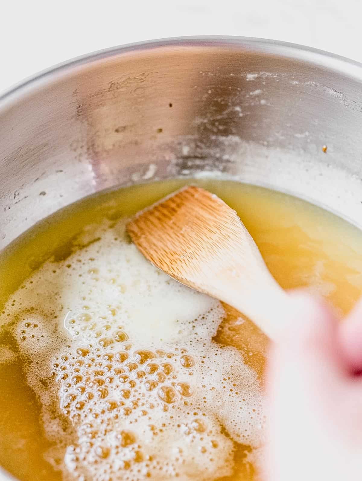 Butter browning in a saucepan with a wooden spoon stirring, creating a golden foam.