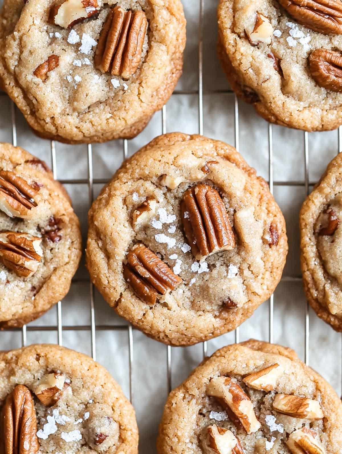 Maple brown sugar pecan cookies with flaky sea salt cooling on a wire rack.