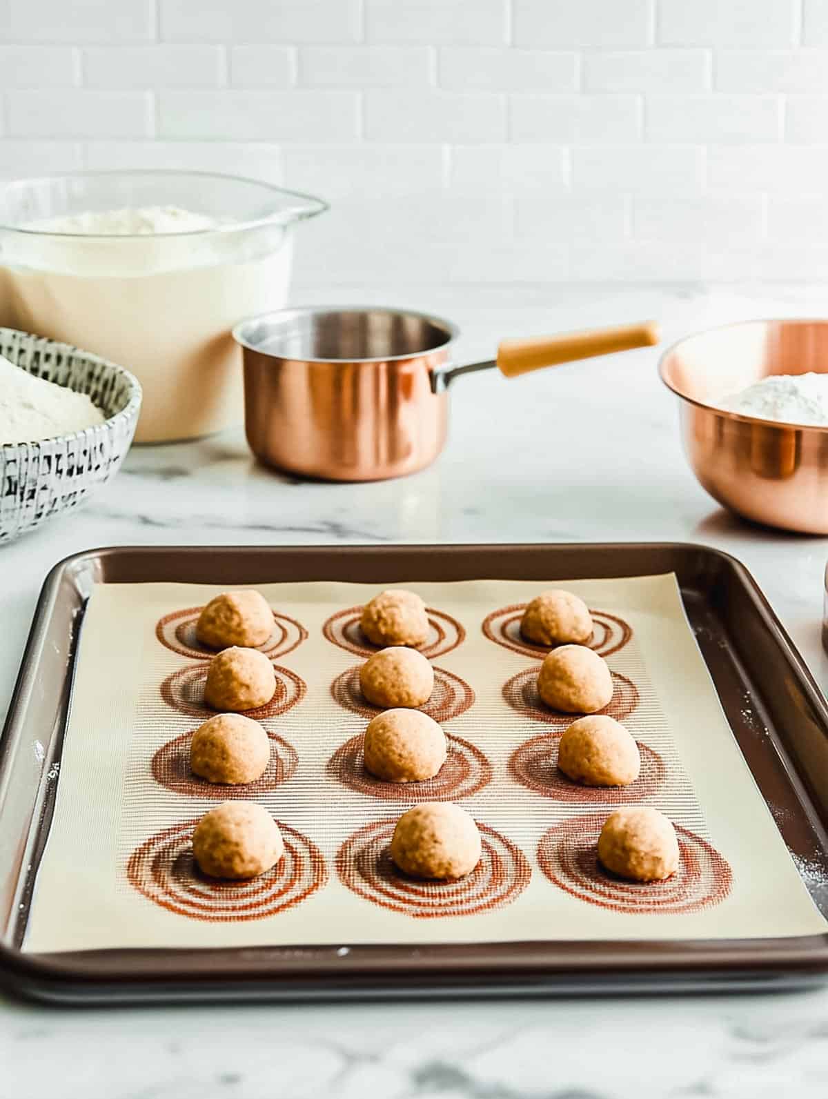 Raw cookie dough balls spaced evenly on a silicone baking mat, ready for the oven.