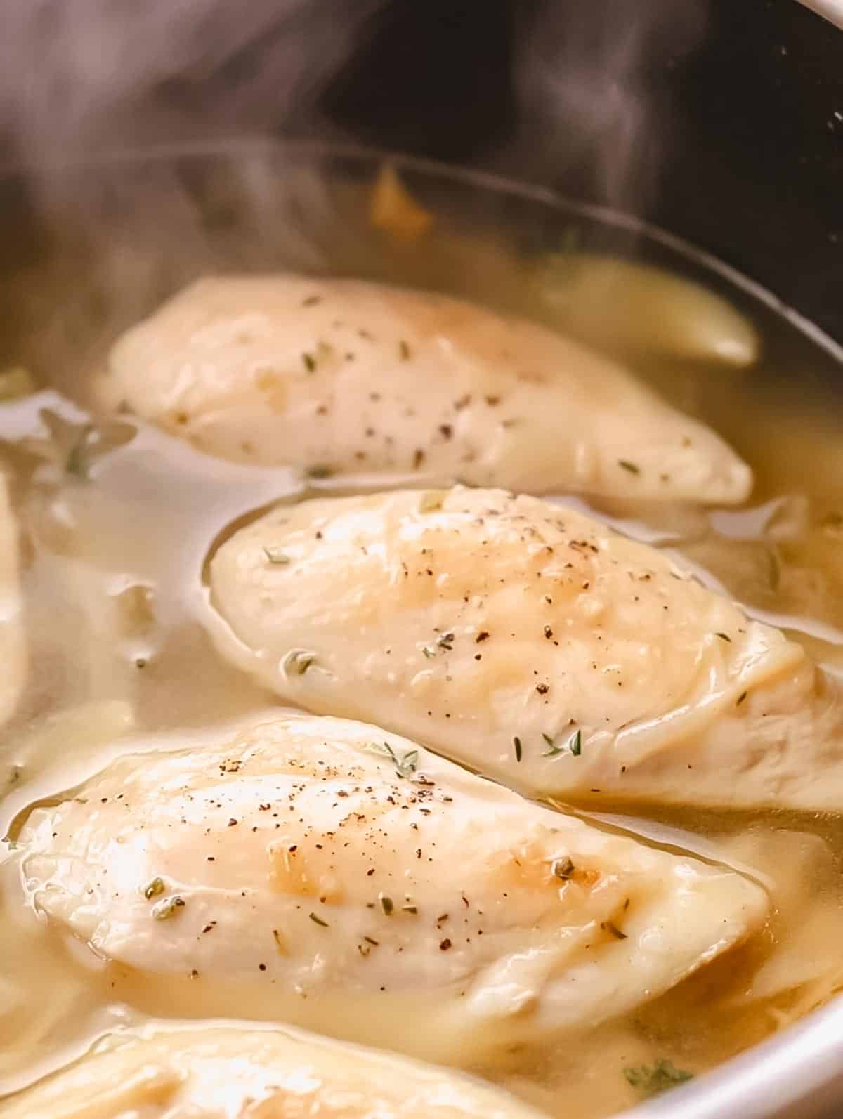 Chicken breasts simmering in a pot of seasoned broth.