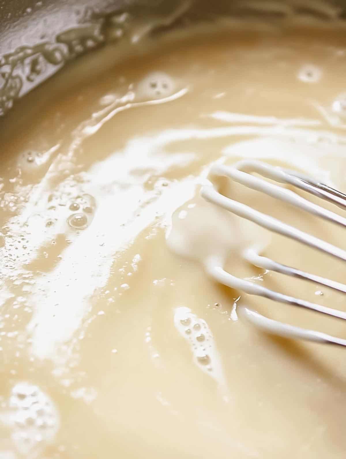 A smooth and creamy roux being whisked in a saucepan.