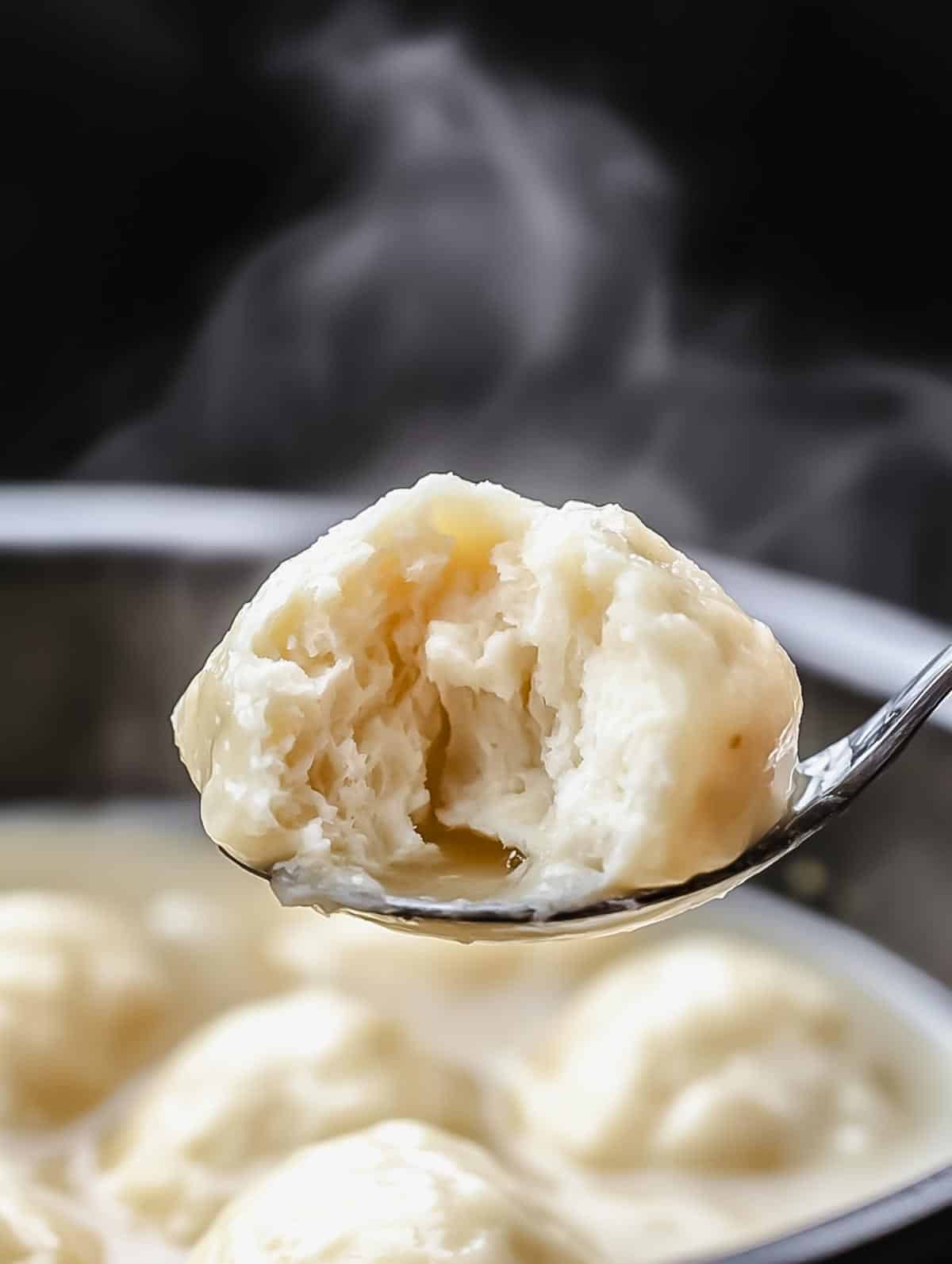 A close-up of a perfectly cooked dumpling with a fluffy interior, held on a spoon above the soup.