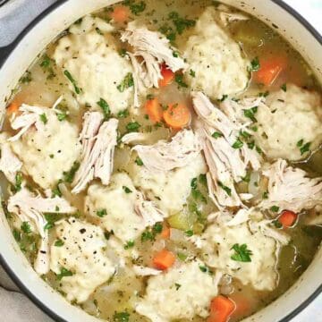 A Dutch oven filled with chicken and dumpling soup, featuring shredded chicken, fluffy dumplings, and carrots in a flavorful broth.