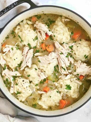 A Dutch oven filled with chicken and dumpling soup, featuring shredded chicken, fluffy dumplings, and carrots in a flavorful broth.