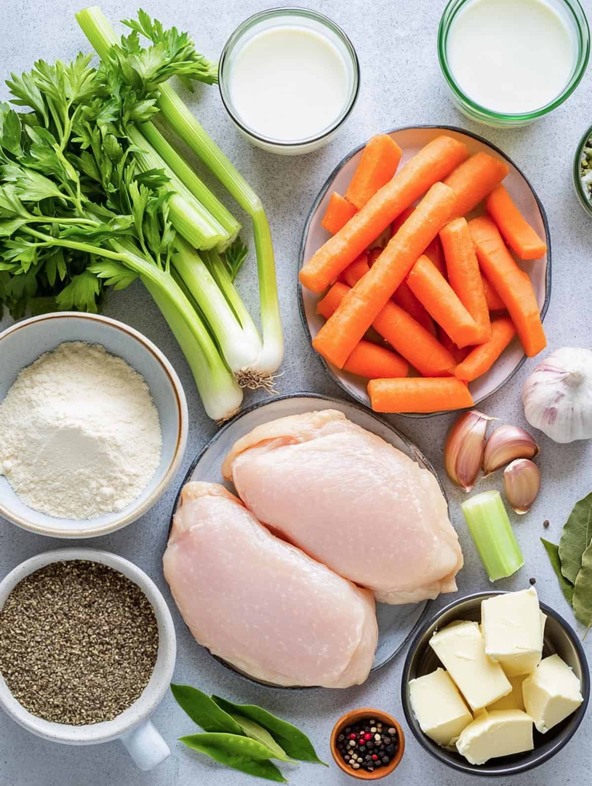 A colorful array of ingredients for chicken and dumpling soup, including fresh celery, carrots, chicken breasts, butter, garlic, and spices.